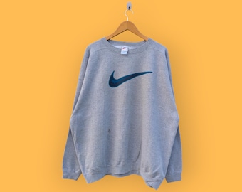 Sudadera Nike vintage de los años 90 con el logo central del gran swoosh. Sudadera Nike de cuello redondo, estilo deportivo, color gris, talla extragrande.