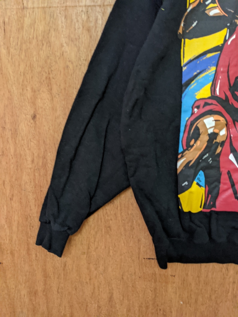 May include: Black sweatshirt with a colorful graphic print of a person wearing a red shirt and a yellow hat. The graphic is in a cartoon style.