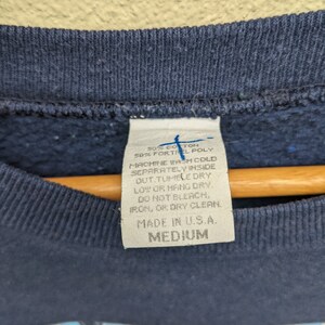 May include: A navy blue sweatshirt with a white tag that reads "50% Cotton 50% Fortrel Poly" and "Machine Wash Cold Separately Inside Out. Tumble Dry Low or Hang Dry. Do Not Bleach, Iron, or Dry Clean. Made in U.S.A. Medium".