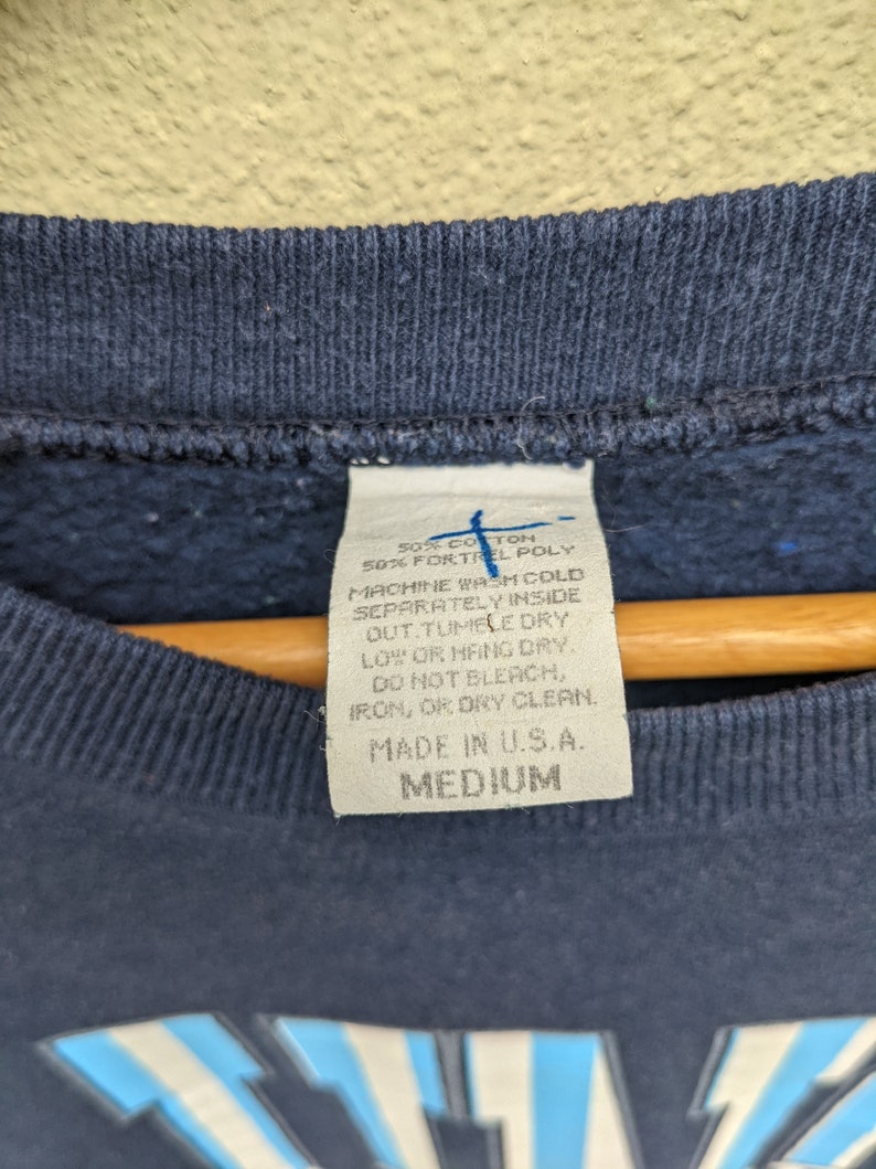 May include: A navy blue sweatshirt with a white tag that reads "50% Cotton 50% Fortrel Poly" and "Machine Wash Cold Separately Inside Out. Tumble Dry Low or Hang Dry. Do Not Bleach, Iron, or Dry Clean. Made in U.S.A. Medium".