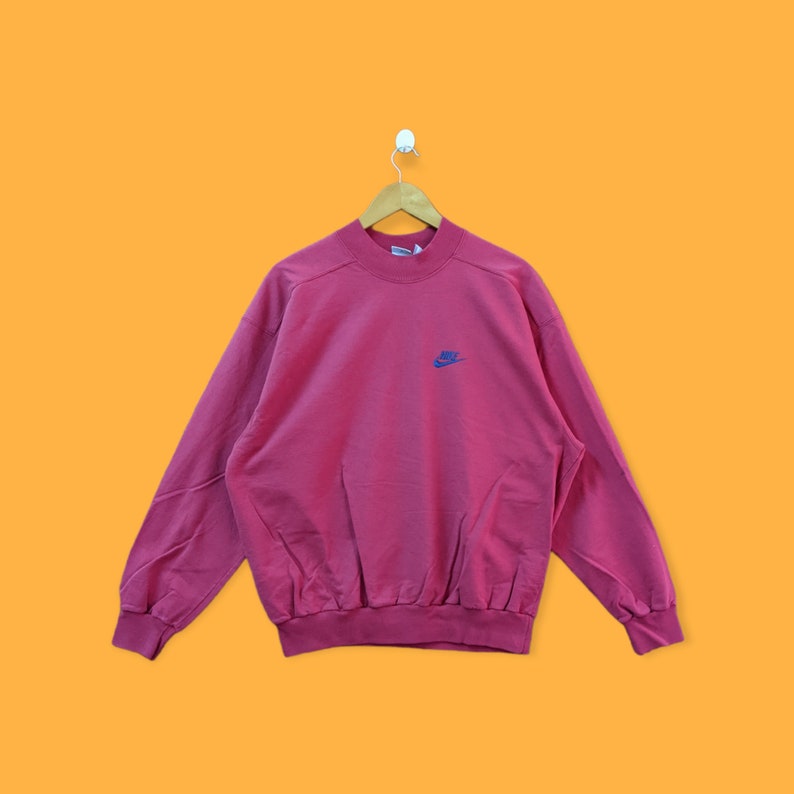 May include: A pink vintage Nike sweatshirt with a blue and white logo.