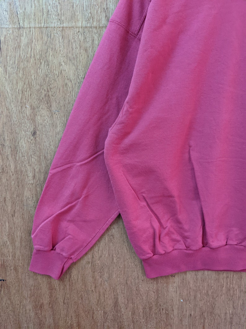 May include: A close-up of the sleeve and bottom hem of a red sweatshirt. The sweatshirt has a ribbed cuff and hem.