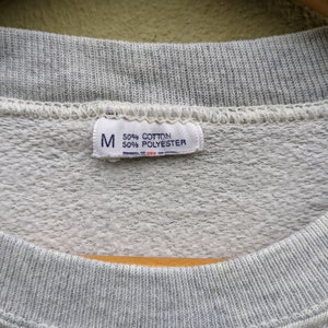 May include: A gray sweatshirt tag with the letter "M" and the text "50% Cotton 50% Polyester".