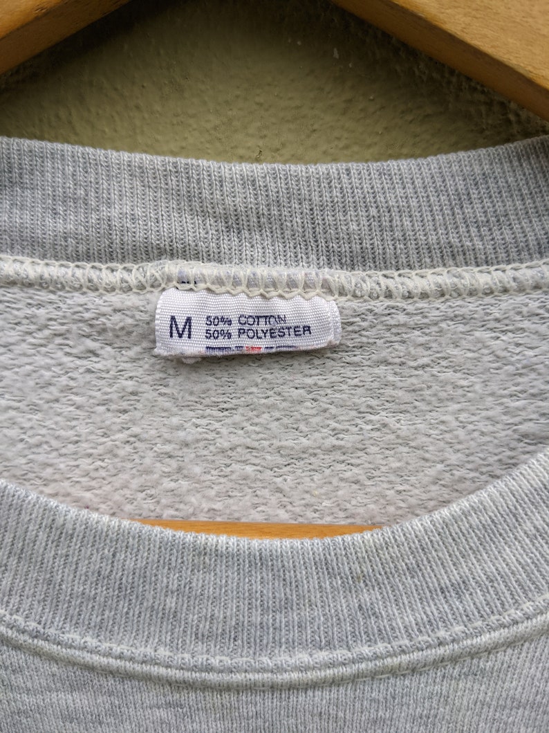 May include: A gray sweatshirt tag with the letter "M" and the text "50% Cotton 50% Polyester".