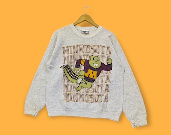May include: Gray sweatshirt with a cartoon squirrel wearing a purple and gold jersey with the letter "M" on it. The squirrel is running and the text "MINNESOTA" is repeated down the front of the sweatshirt.