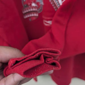 May include: Close-up of the red ribbed cuff of a long-sleeved shirt. The cuff is folded over twice, showing the inside of the fabric.