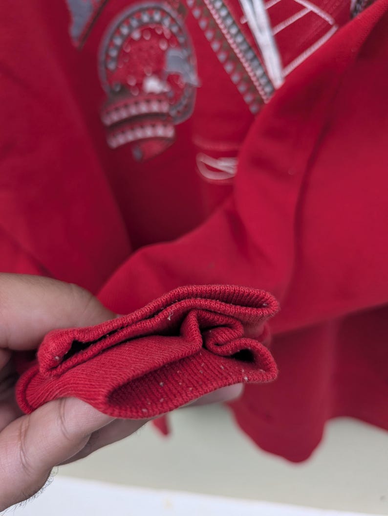 May include: Close-up of the red ribbed cuff of a long-sleeved shirt. The cuff is folded over twice, showing the inside of the fabric.