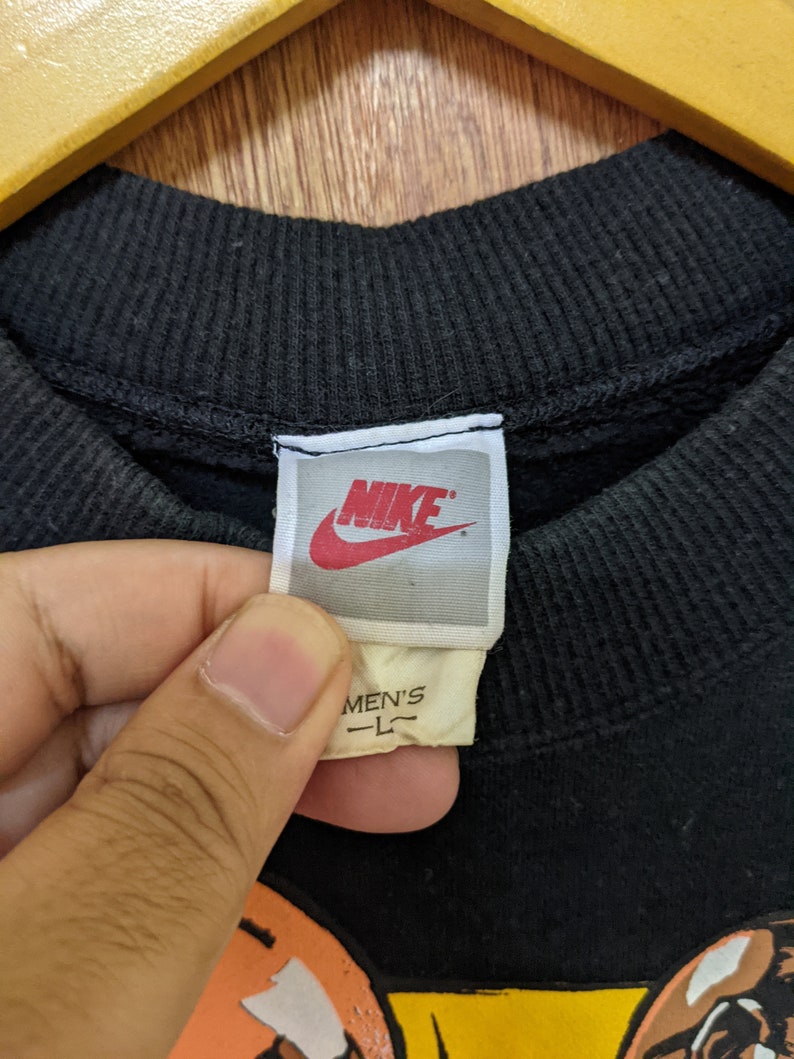May include: Black sweatshirt with a Nike logo and the text "MEN'S L" on the tag. The sweatshirt features a cartoon graphic of two people.