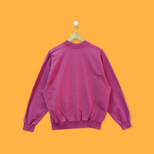 May include: A pink sweatshirt with long sleeves and a crew neck.