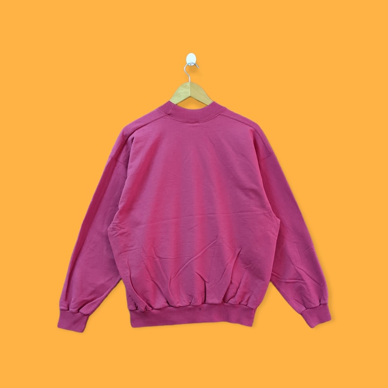 May include: A pink sweatshirt with long sleeves and a crew neck.