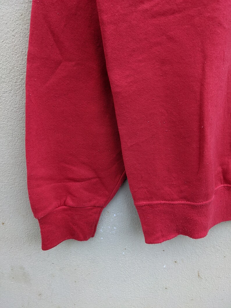 May include: A red sweatshirt with long sleeves and a ribbed cuff. The sweatshirt is made of a soft, comfortable fabric.
