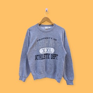 Könnte beinhalten: Grauer Sweatshirt mit einem weißen und marineblauen Aufdruck, der "Property of U.S. Navy" lautet, mit einem marineblauen Oval, auf dem "XXL" und "Athletic Dept." steht.