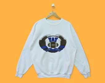 May include: White sweatshirt with a blue and brown graphic of a football and a wreath with the letters "W" and "T" inside. The text "EST. 1950" is below the graphic.