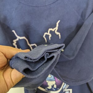 May include: Navy blue sweatshirt with white lightning bolt graphics and a collegiate emblem. The emblem features a cartoon bear wearing a sweater and the text "GO TAR HEELS". The sweatshirt has a crew neck and long sleeves.