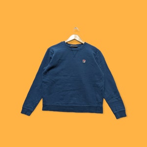 May include: A dark blue sweatshirt with a small embroidered logo on the left chest. The logo is red, white, and blue.