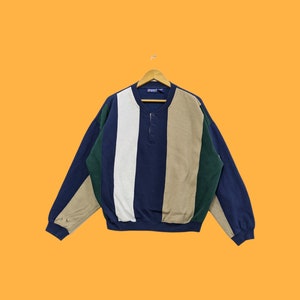 Puede incluir: Un suéter de rayas de manga larga con cuello de botones. El suéter es azul, verde, blanco y beige.