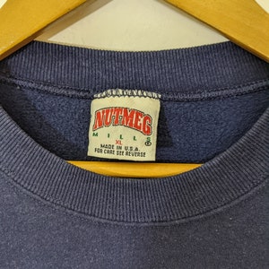 Peut inclure: Un sweat-shirt bleu marine avec une &eacute;tiquette blanche sur laquelle est inscrit "Nutmeg" et les tailles "M", "L", "XL" et "S". L'&eacute;tiquette indique &eacute;galement "Made in U.S.A. For care see reverse."