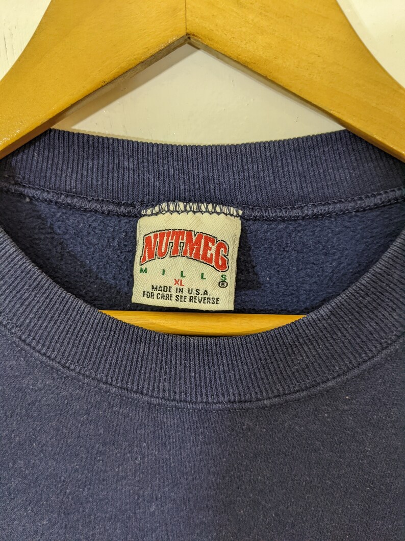 Peut inclure: Un sweat-shirt bleu marine avec une &eacute;tiquette blanche sur laquelle est inscrit "Nutmeg" et les tailles "M", "L", "XL" et "S". L'&eacute;tiquette indique &eacute;galement "Made in U.S.A. For care see reverse."