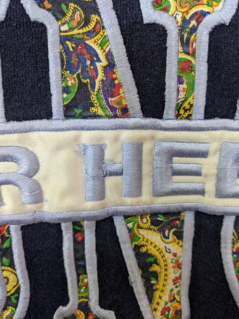 Peut inclure: Un sweat-shirt bleu marine avec un patch blanc sur lequel est brod&eacute; en bleu "HER HEART". Le patch est entour&eacute; d'un motif paisley bleu.