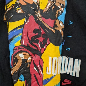 May include: Black sweatshirt with a colorful graphic of a basketball player dribbling a ball. The graphic includes the text "AIR JORDAN" and the Nike swoosh logo.