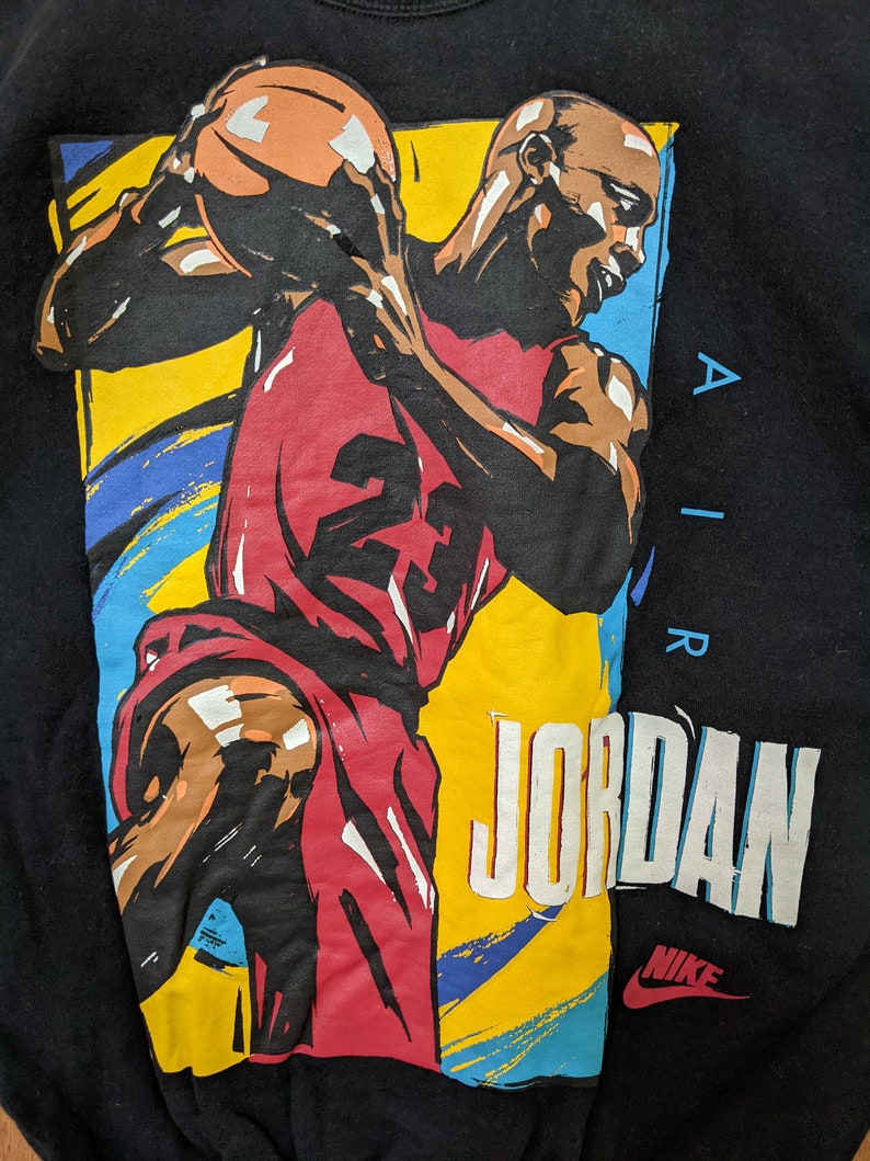 May include: Black sweatshirt with a colorful graphic of a basketball player dribbling a ball. The graphic includes the text "AIR JORDAN" and the Nike swoosh logo.
