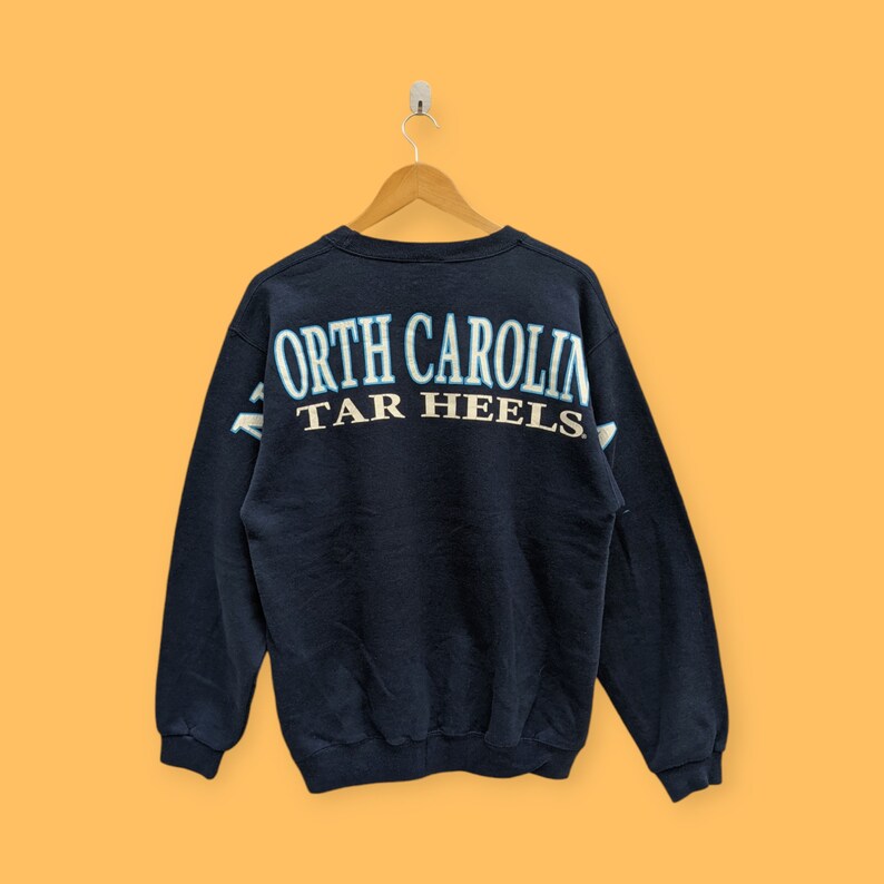 May include: A navy blue sweatshirt with the text "North Carolina Tar Heels" in white and light blue lettering on the back.