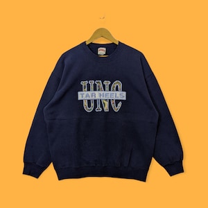 Peut inclure: Un sweat-shirt bleu marine avec un grand patch brod&eacute; qui dit "UNC TAR HEELS UNC" dans un motif floral color&eacute;.