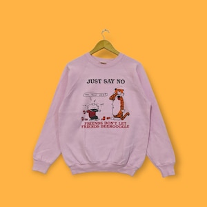 Könnte beinhalten: Rosafarbener Pullover mit einem Cartoon-Bild von Calvin und Hobbes. Der Text auf dem Pullover lautet "Just Say No" und "Friends Don't Let Friends Beer Goggle."