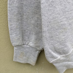 May include: Close-up of the gray fabric cuff of a sweatshirt. The fabric is slightly textured and has a subtle ribbed pattern.