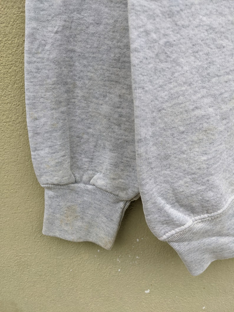 May include: Close-up of the gray fabric cuff of a sweatshirt. The fabric is slightly textured and has a subtle ribbed pattern.