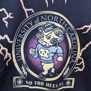 May include: Navy blue sweatshirt featuring a University of North Carolina Tar Heels graphic. The design includes a cartoon ram mascot in a light blue sweater, the words "University of North Carolina," and "Go Tar Heels!" in gold lettering, with lightning bolt accents.