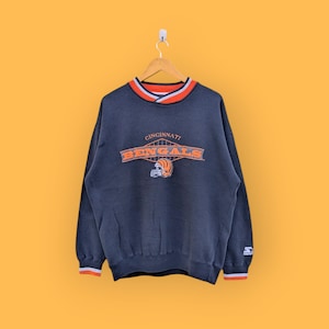 May include: A navy blue Cincinnati Bengals sweatshirt with orange and white trim on the collar and cuffs. The Bengals logo and text are in orange. The sweatshirt is hanging on a wooden hanger.