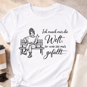 Puede incluir: Camiseta blanca con un dibujo negro de una mujer sentada en un banco, mostrando el dedo coraz&oacute;n. El texto en alem&aacute;n dice "Ich mach mir die Wett, so wie sie mir gef&auml;llt..."