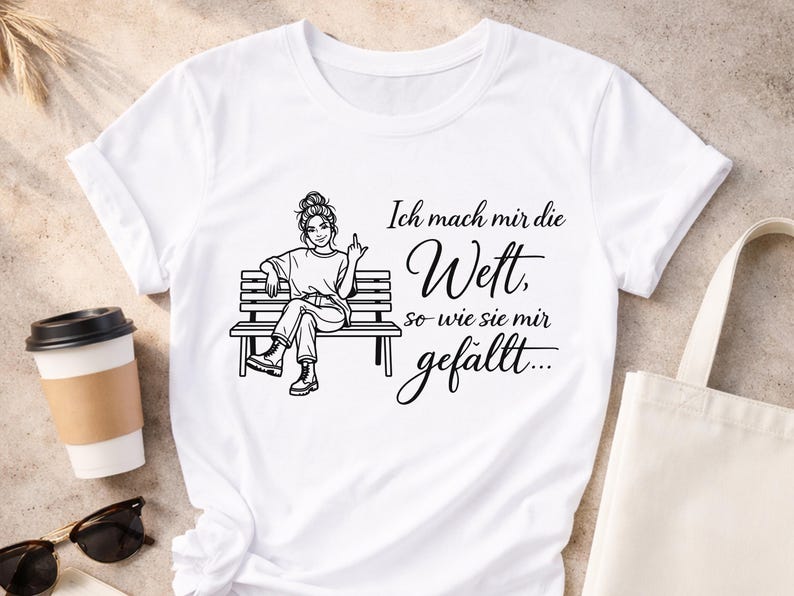 Puede incluir: Camiseta blanca con un dibujo negro de una mujer sentada en un banco, mostrando el dedo coraz&oacute;n. El texto en alem&aacute;n dice "Ich mach mir die Wett, so wie sie mir gef&auml;llt..."