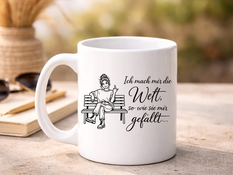 Puede incluir: Taza de cer&aacute;mica blanca con una ilustraci&oacute;n negra de una persona sentada en un banco, mostrando el dedo medio. La taza tiene el texto alem&aacute;n "Ich mach mir die Wett, so wie sie mir gef&auml;llt..."