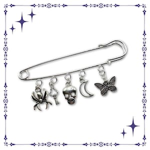 Puede incluir: Un imperdible plateado con colgantes. Los colgantes incluyen una araña, una llave, una calavera, una luna creciente y una mariposa. Accesorio decorativo.