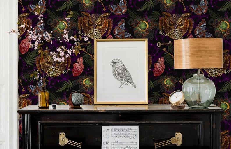 May include: A black and purple wallpaper with a repeating pattern of owls, hearts, keys, and butterflies. The wallpaper is displayed on a black piano with sheet music on top. A framed drawing of a bird is on the piano, and a lamp with a wooden base and a clear glass shade is on the piano.