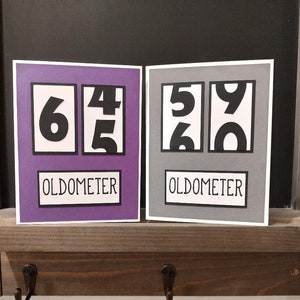 May include: Two purple and gray cards with black numbers on them. The cards have the word "Oldometer" printed on them. The numbers on the cards are 645 and 590.