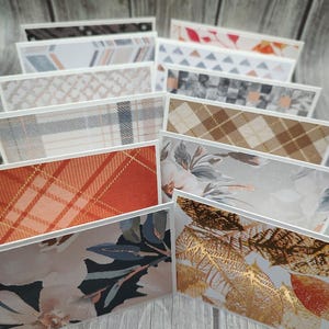 May include: A stack of blank greeting cards with various patterns, including plaid, floral, geometric, and abstract designs. The cards are all white with a white border and are arranged in a fan shape.