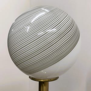 May include: A spherical lamp with a white and gray striped glass shade. The shade is mounted on a brass-colored metal base. The lamp has a modern design and is suitable for home decor.