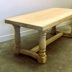 May include: A rustic wooden coffee table with a natural wood finish. The table has a rectangular top and four turned legs with a stretcher connecting the legs.