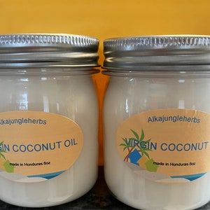 May include: Two glass jars with silver lids filled with white virgin coconut oil. The jars have yellow labels with the text "Alkajungleherbs Virgin Coconut Oil made in Honduras 8oz."