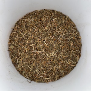 Könnte beinhalten: Nahaufnahme von getrockneten Kräutern, die einen weißen Behälter füllen. Die Kräuter sind eine Mischung aus Grün, Braun und Beige, mit einer Vielzahl von Texturen von kleinen Blättern bis zu dünnen Stängeln. Das Bild ist gut beleuchtet.