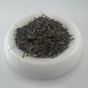 May include: A white bowl filled with dried green leaves and stems.