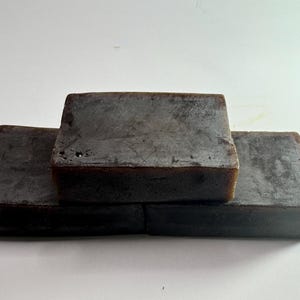 May include: Three rectangular bars of dark brown soap stacked on top of each other.