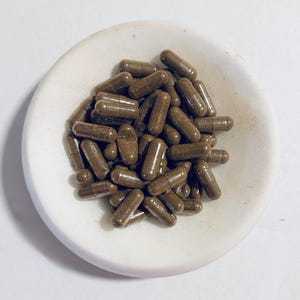 May include: A white ceramic dish filled with brown capsules. The capsules are a natural brown color and are all the same size and shape.