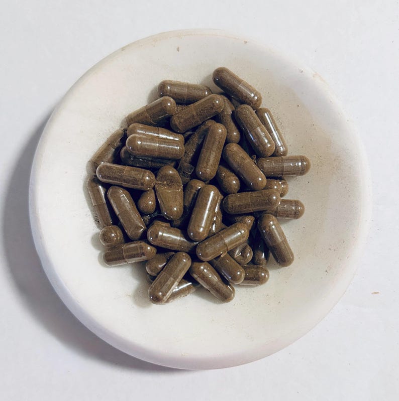May include: A white ceramic dish filled with brown capsules. The capsules are a natural brown color and are all the same size and shape.