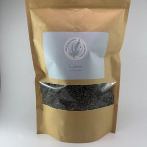 May include: A brown paper bag with a white label that says "AlcaJungleHerbs" and "Chanca" with a drawing of a plant. The bag contains dried herbs.