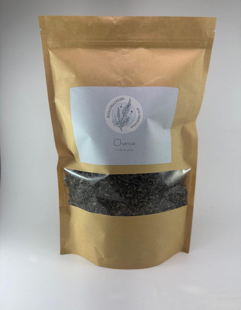 May include: A brown paper bag with a white label that says "AlcaJungleHerbs" and "Chanca" with a drawing of a plant. The bag contains dried herbs.