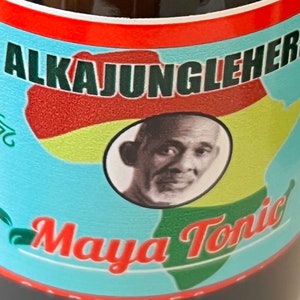 May include: A bottle of dark liquid with a label that says "AlkaJungleHerbs Maya Tonic". The label features a map of Africa in red, yellow, and green, with a portrait of a man in the center.